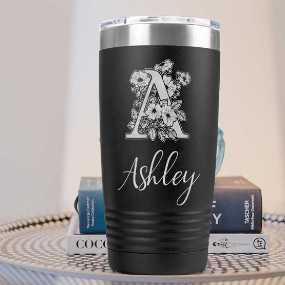Custom Black Coffee Tumbler Laser Engraved With Ashley And Initial Inside Flower Artwork On A Side Table With Books