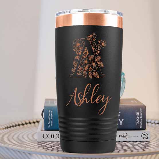 Black And Rose Gold Twenty Ounce Coffee Tumbler Engraved With Name And Monogram And Flower Art On A Side Table With Books