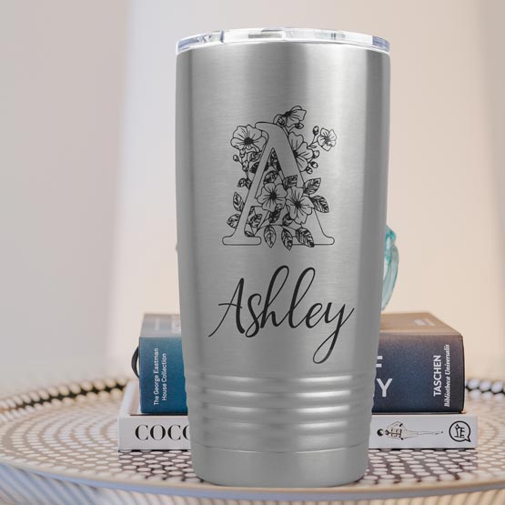Twenty Ounce Stainless Steel Coffee Tumbler Engraved With Ashley And Monogram And Flower Art On Table With Books