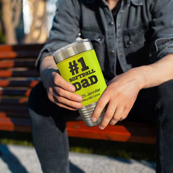 Man On Bench Holding Faux Leather Wrapped Coffee Tumbler With Softball Theme And Engraved With Number One Dad Message
