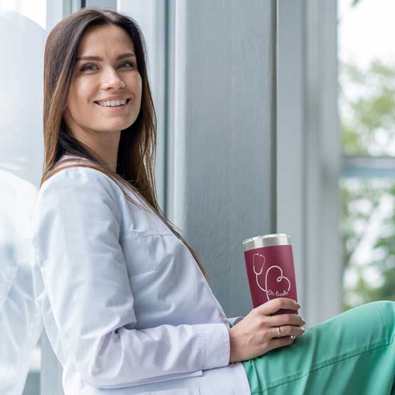 Nurse Sitting Against Window Holding Maroon 20 Ounce Stainless Steel Tumbler Engraved With Name Inside Stethoscope Art
