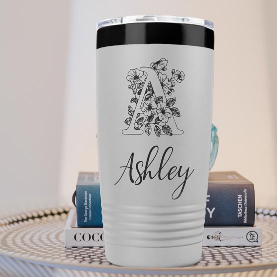 White And Black Twenty Ounce Coffee Tumbler Engraved With Ashley And Monogram And Flower Art On Table With Books
