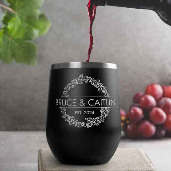 Wine Bottle Pouring Wine Into Black Stemless Wine Tumbler Engraved With Couple Names And Wheat Art On A Kitchen Counter