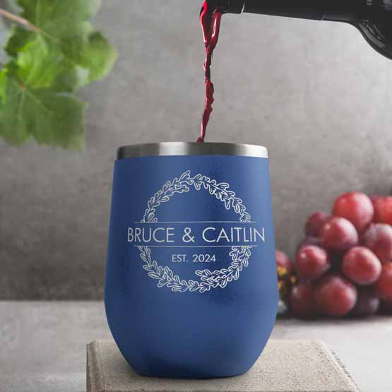 Wine Bottle Pouring Wine Into Blue Stemless Wine Tumbler Engraved With Couple Names And Wheat Art On A Kitchen Counter