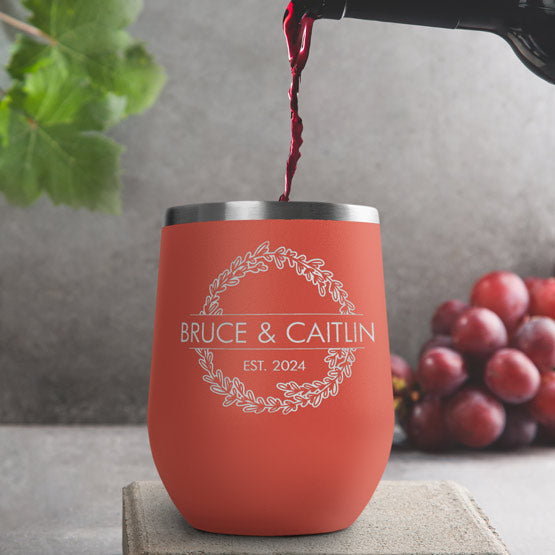 Wine Bottle Pouring Wine Into Coral Stemless Wine Tumbler Engraved With Couple Names And Wheat Art On A Kitchen Counter