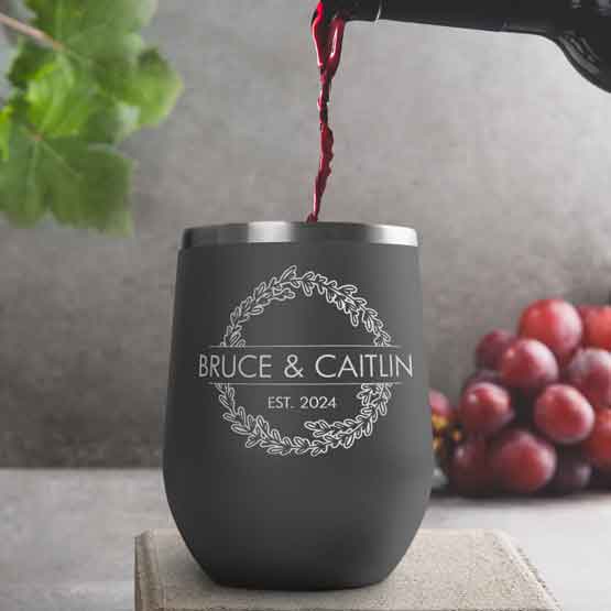 Wine Bottle Pouring Wine Into Gray Stemless Wine Tumbler Engraved With Couple Names And Wheat Art On A Kitchen Counter
