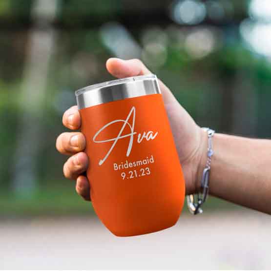 Woman Hand Outdoors Holding Custom Orange Stemless Wine Tumbler Engraved With Name And Date And Bridesmaid Text