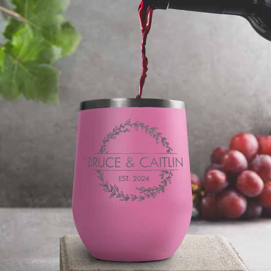 Wine Bottle Pouring Wine Into Pink Stemless Wine Tumbler Engraved With Couple Names And Wheat Art On A Kitchen Counter
