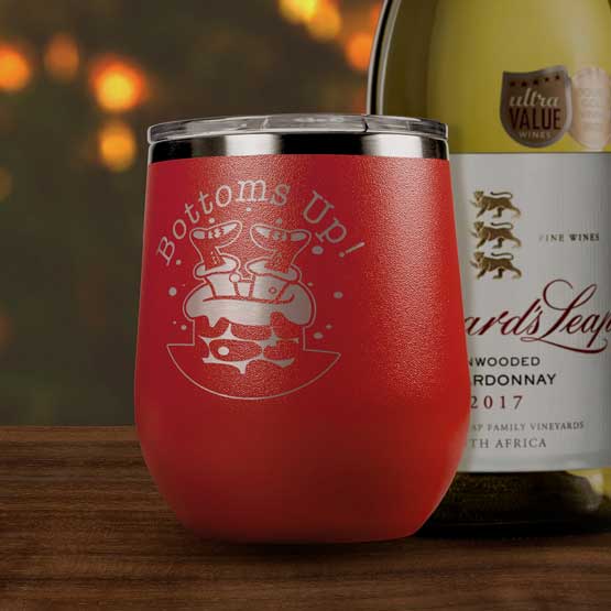 Red 12 Ounce Stemless Wine Tumbler Engraved With Bottoms Up Text And Santa Going Down Chimney Art On Table Beside Wine Bottle