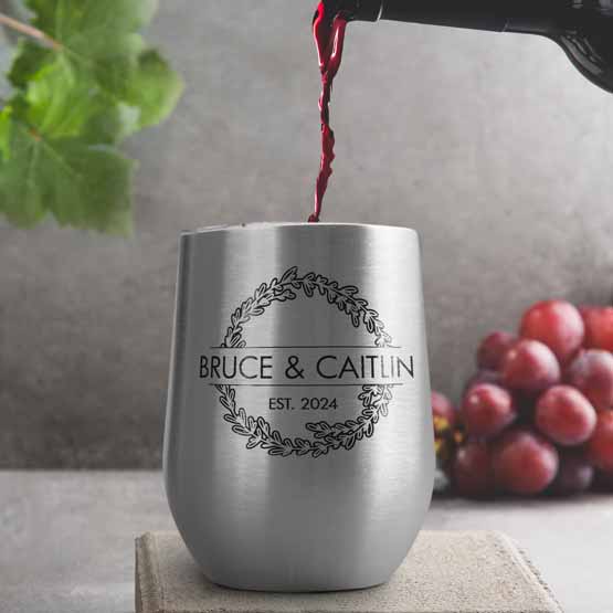 Wine Bottle Pouring Wine Into Silver Stemless Wine Tumbler Engraved With Couple Names And Wheat Art On A Kitchen Counter