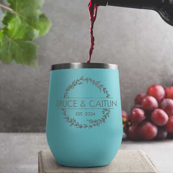 Wine Bottle Pouring Wine Into Teal Stemless Wine Tumbler Engraved With Couple Names And Wheat Art On A Kitchen Counter