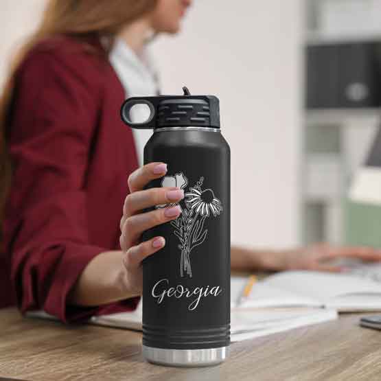 Woman At Office Desk Holding Black Thirty Two Ounce Water Bottle With Straw And Laser Engraved With Name And Flower Art