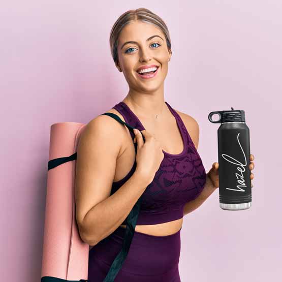 Woman In Workout Clothes Carrying Yoga Mat And Black Thirty Two Ounce Water Bottle With Straw And Engraved With Name
