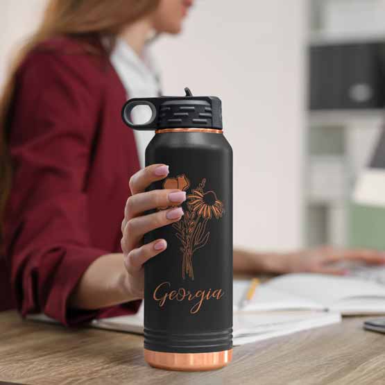 Woman At Office Desk Holding Black And Rose Gold Thirty Two Ounce Water Bottle With Straw And Engraved Name And Flower Art