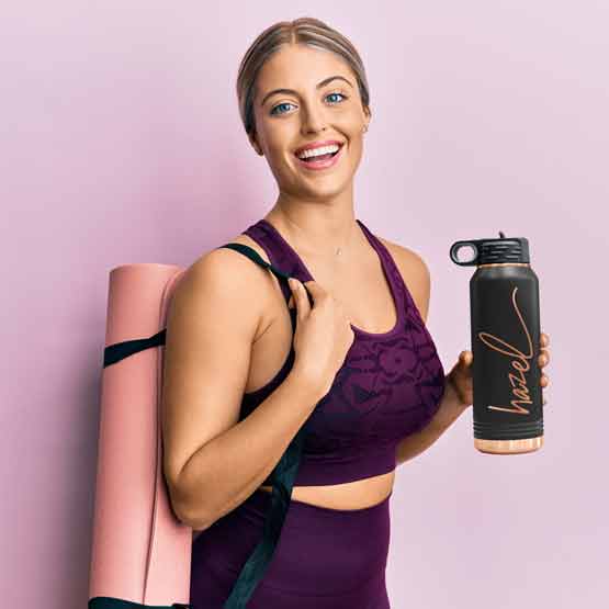Woman In Workout Clothes Carrying Yoga Mat And Black And Rose Gold Thirty Two Ounce Water Bottle With Straw And Engraved Name