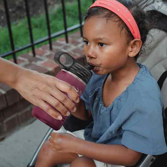 Hand Serving Maroon Stainless Steel Child Water Bottle With Straw And Engraved Name To Little Girl In Stroller Outdoors