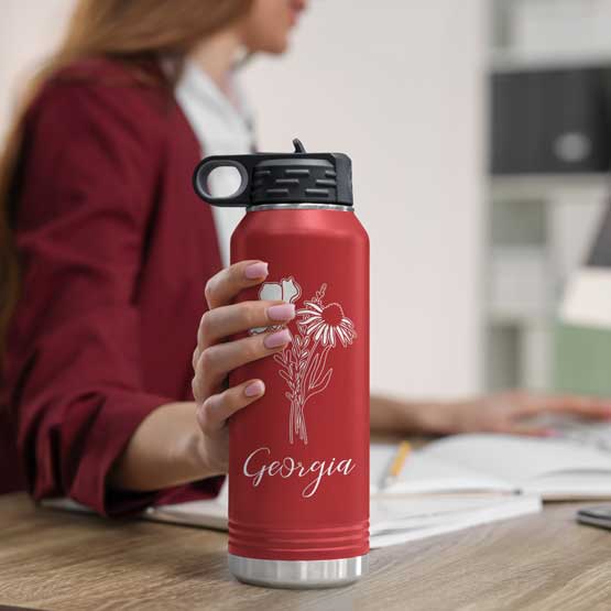 Woman At Office Desk Holding Red Thirty Two Ounce Water Bottle With Straw And Laser Engraved With Name And Flower Art