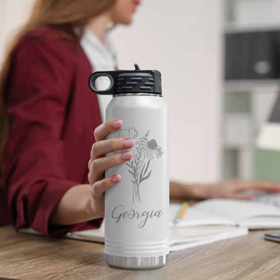 Woman At Office Desk Holding White Thirty Two Ounce Water Bottle With Straw And Laser Engraved With Name And Flower Art