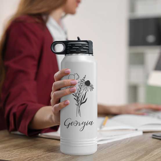 Woman At Office Desk Holding White And Black Thirty Two Ounce Water Bottle With Straw And Engraved With Name And Flower Art