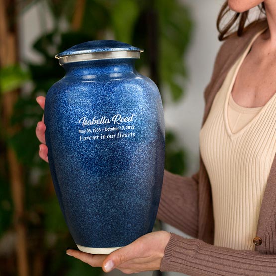 Woman Indoors Near A Plant And Holding Blue Aluminum Cremation Urn Engraved With Custom Memorial Details And Message