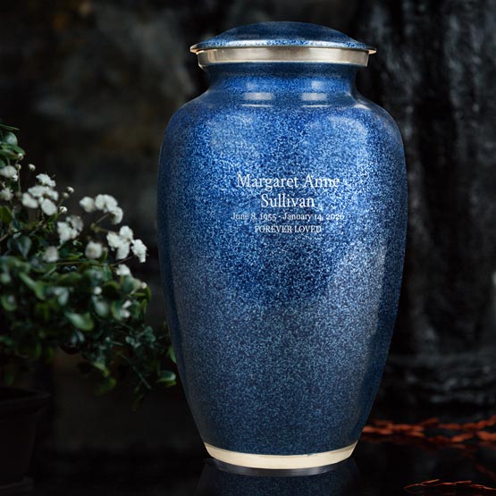 Blue Aluminum Cremation Urn Engraved With Custom Memorial Details And Message Sitting On A Table Beside White Flowers