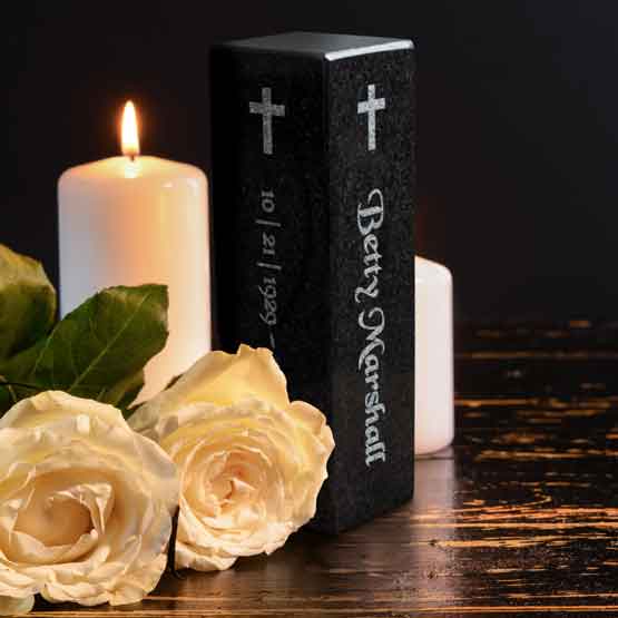 Custom Granite Pillar In Portrait Layout And Engraved With Cross Art And Memorial Details On Table With Candles And Flowers