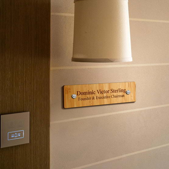 Custom Bamboo Office Name Plate Engraved With Founder Details Mounted On Office Wall Via Two Silver Standoffs