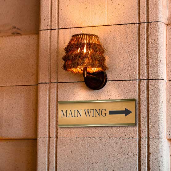 Bronze Office Name Plate Laser Fused With Main Wing Text And Arrow Art Mounted On Wall Beneath Sconce Via Gold Bracket