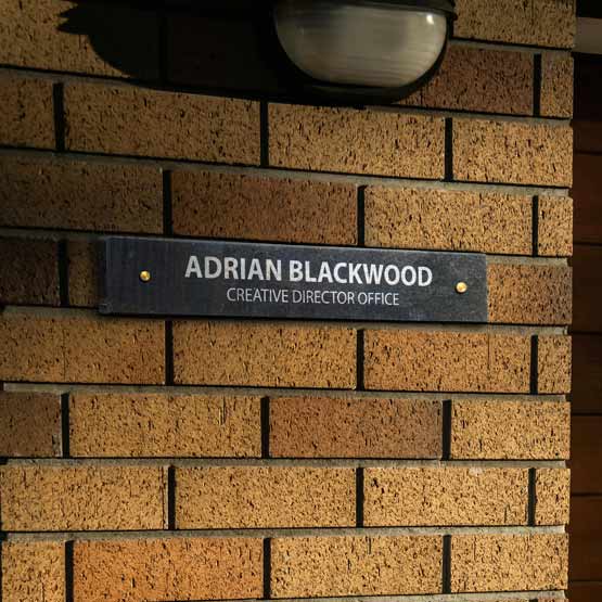 Custom Granite Office Plate Engraved With Creative Director Name And Title Mounted Onto Brick Wall Via Two Gold Standoffs