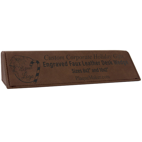 A faux brown leather desk wedge sitting at an angle with text engraved on the front detailing the desk’s features, set on a white background.