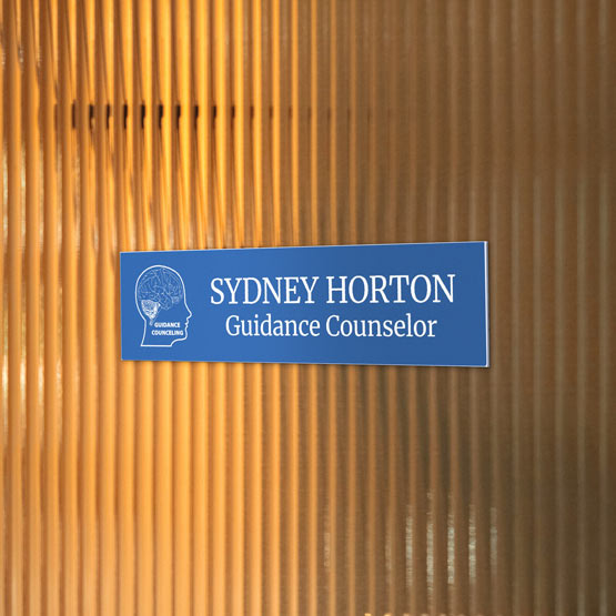 A sky blue plastic name plate read ‘Sydney Horton Guidance Counselor’ with a white head icon, mounted on a warm amber ribbed glass door.