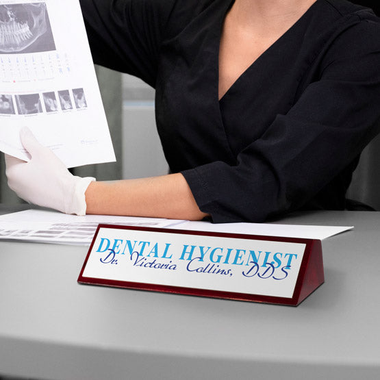 Dental hygienist at a desk with a nameplate displaying 'Dental Hygienist Dr. Victoria Collins, DDS'.
