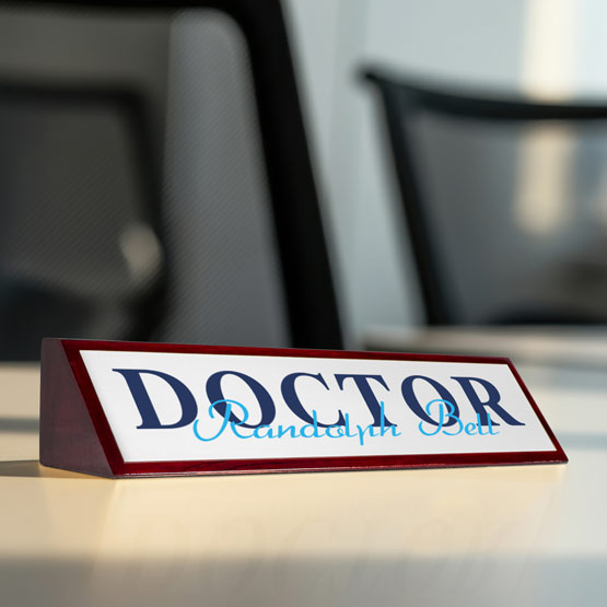Desk nameplate with 'DOCTOR' and a name on it, placed on a surface with a blurred background.