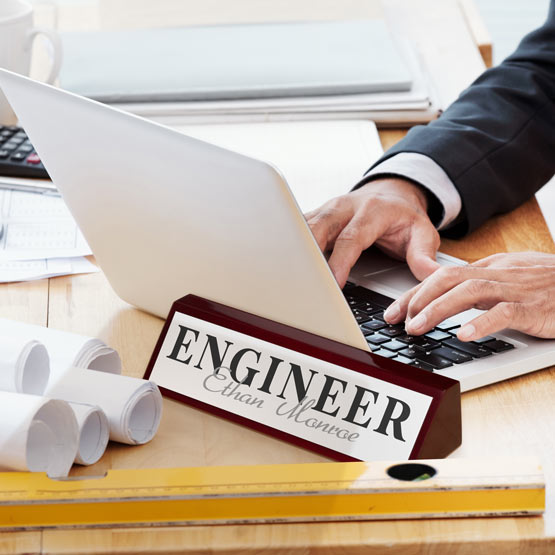 Person typing on a laptop with a custom 'Engineer' nameplate on a desk