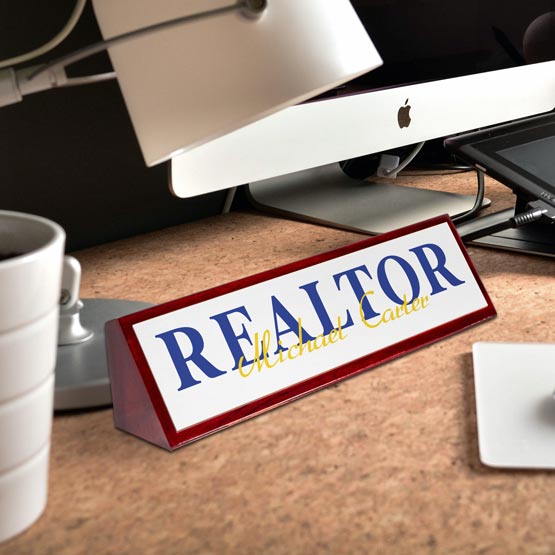 Personalized 'REALTOR' nameplate on a desk with a computer and coffee cup in the background.