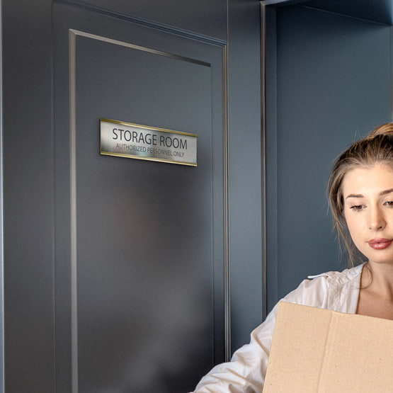 Woman Carrying Box Past Door With Stainless Steel Office Plate Laser Fused With Storage Room Details Mounted Via Gold Bracket