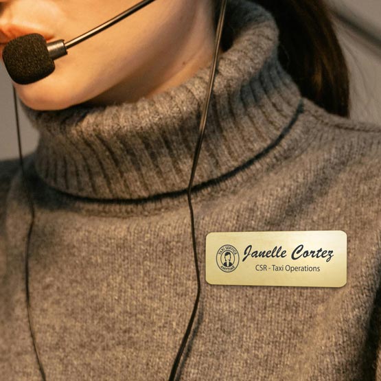 Woman Wearing Headset And Sweater And Brass Magnetic Name Badge Laser Fused With Taxi Operations Logo And Employee Details