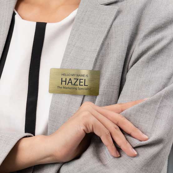Woman Wearing Custom Engraved Brass Name Tag With The Name Hazel On Gray Suit Jacket. 