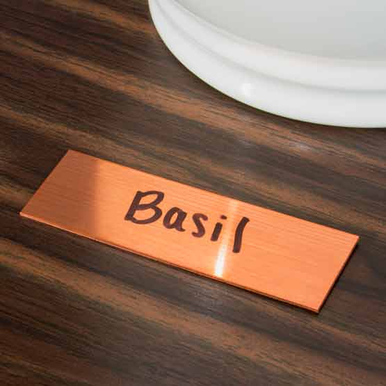 Custom Copper Name Tag With Rectangle Shape And Marked With Handwritten Basil Text In Black On A Wood Desk With Decor