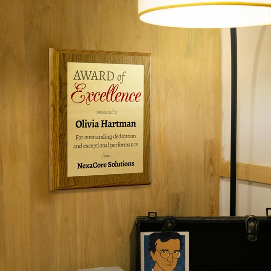 Award of Excellence Plaque For Olivia Hartman On Wooden Wall Beneath Floor Lamp
