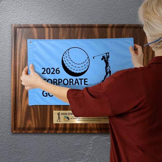 Woman Hanging Blue Golf Flag Onto Walnut Plaque With Gold Plate Printed With Golf Award Message And Mounted On A Wall