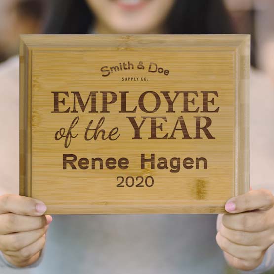 Woman Holding Up Solid Bamboo Plaque Engraved With Award Message For Employee Of The Year With Name And Date