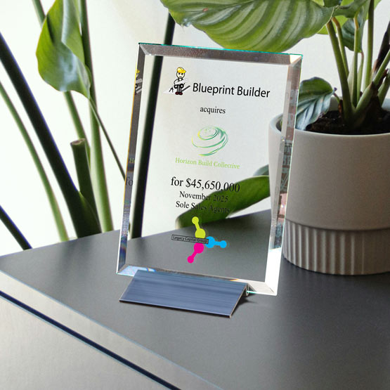 A clear glass plaque award on a small black stand, displaying the Blueprint Builder logo and text, set on a dark tabletop next to a potted green plant.