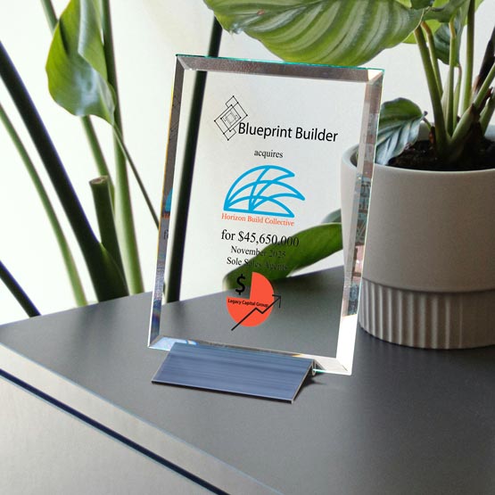 A clear glass plaque award on a small black stand, displaying the Blueprint Builder logo and text, set on a dark tabletop next to a potted green plant.