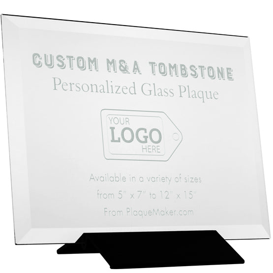 A clear personalized glass tombstone plaque displayed on a black stand against a white background with engraved text and a placeholder artwork.