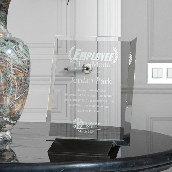 Engraved Glass Plaque Award For Employee Of The Month With Logo And Message And Black Base On Marble Table With Vase