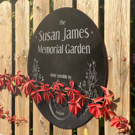 Granite Circle Plaque Engraved With Susan James Memorial Garden Message And Flower Art On Wood Fence With Red Flowers