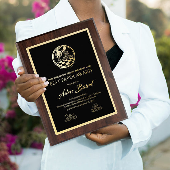 Woman holding a laser engraved plaque with gold engraving for an academic award for “Best Paper”. Outside award ceremony surrounded by flowers.