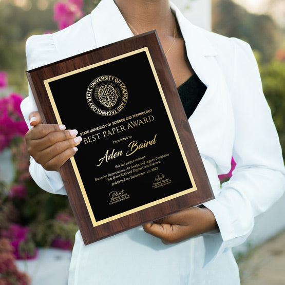 Woman holding a laser engraved plaque with gold engraving for an academic award for “Best Paper”. Outside award ceremony surrounded by flowers.