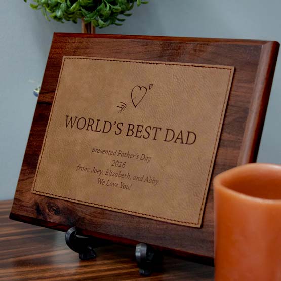 Plaque With Wood Board And Dark Brown Faux Leather Plate With World’s Best Dad Message Standing Via Easel On Shelf With Plant